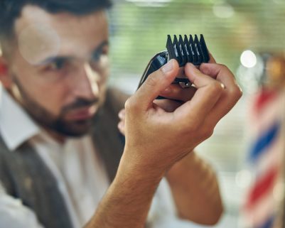 Highly-qualified hair-stylist checking the guards of an electric hair clipper and cleaning it