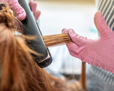 Master is running a iron through the client's hair for keratin straightening. Process of hair care procedures in the salon or at home.